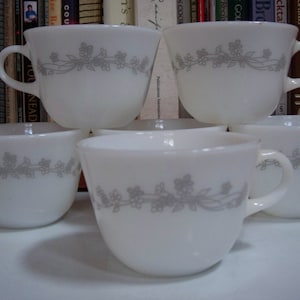 May include: Five white ceramic coffee mugs with a gray floral design. The mugs are stacked on top of each other.