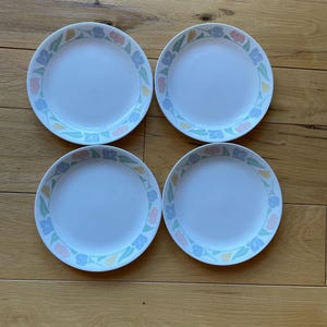 May include: Set of four white ceramic dinner plates with a floral design in shades of blue, pink, and yellow. The plates have a white rim and a floral pattern around the edge.