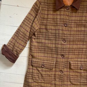 May include: A brown and burgundy plaid jacket with a brown suede collar and cuffs. The jacket has a button closure and two large patch pockets on the front.