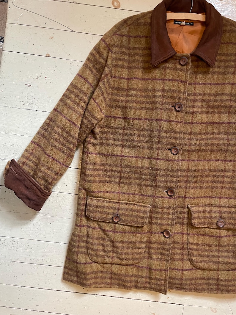 May include: A brown and burgundy plaid jacket with a brown suede collar and cuffs. The jacket has a button closure and two large patch pockets on the front.