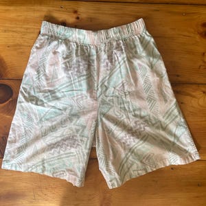May include: Light-colored shorts with an elastic waistband and a geometric pattern in shades of pink, green, and gray. The shorts are made of a lightweight fabric, perfect for warm weather.