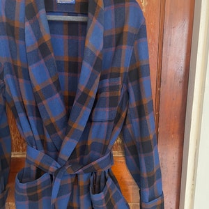 May include: A blue and brown plaid robe with a self-tie belt. The robe has a collar and two pockets. The label on the robe reads "Pendleton."