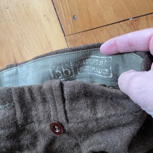 Peut inclure: Gros plan sur un pantalon en laine marron avec un bouton marron et une &eacute;tiquette indiquant "100% laine Fabriqu&eacute; aux &Eacute;tats-Unis."