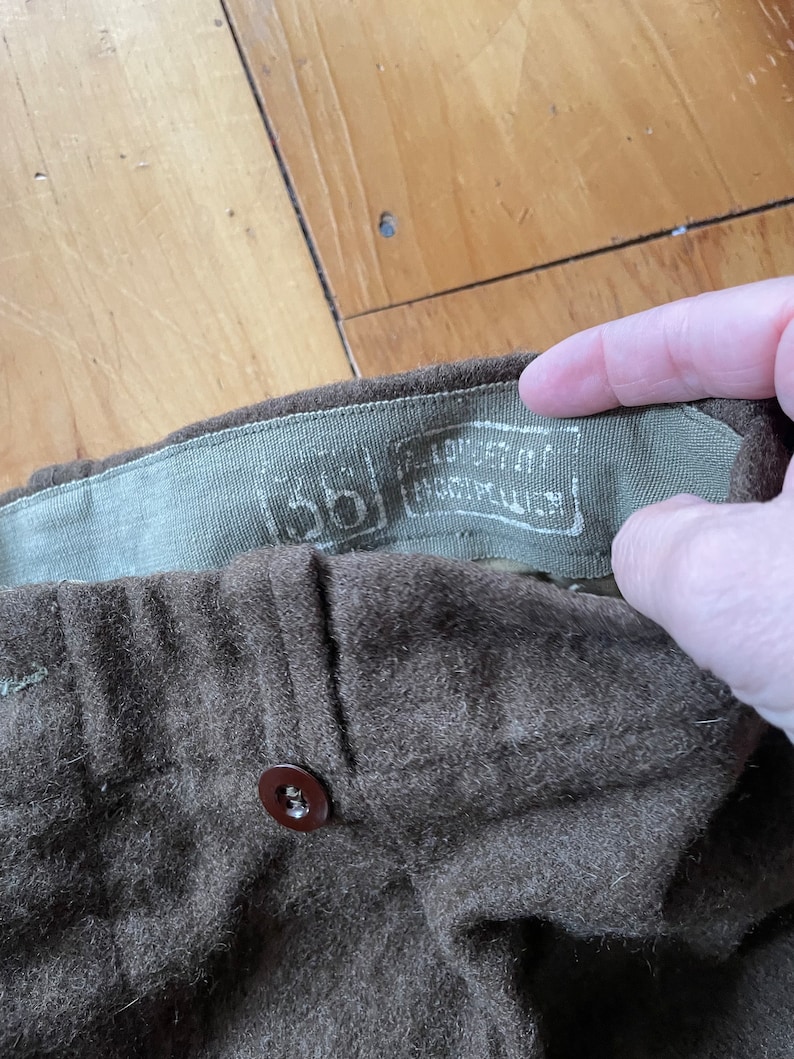 Peut inclure: Gros plan sur un pantalon en laine marron avec un bouton marron et une &eacute;tiquette indiquant "100% laine Fabriqu&eacute; aux &Eacute;tats-Unis."