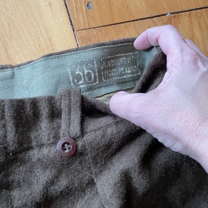 Peut inclure: Un pantalon en laine marron avec un bouton marron et une &eacute;tiquette indiquant "100% EXTRA FINE MERINO WOOL" et "5B".