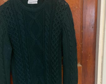 May include: A dark green cable knit sweater with a crew neck.