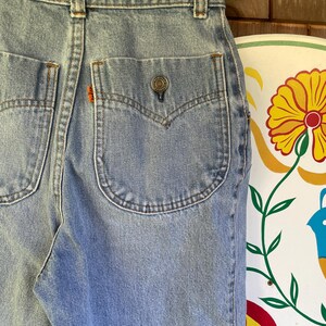 May include: Light blue denim jeans with a button closure and two back pockets. The jeans have a classic, vintage style with a faded wash. The back pocket features a small orange tag.