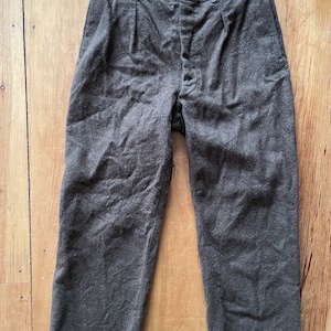 Peut inclure: Un pantalon en laine marron avec une braguette &agrave; boutons et des plis. Le pantalon a une ceinture vert fonc&eacute;.