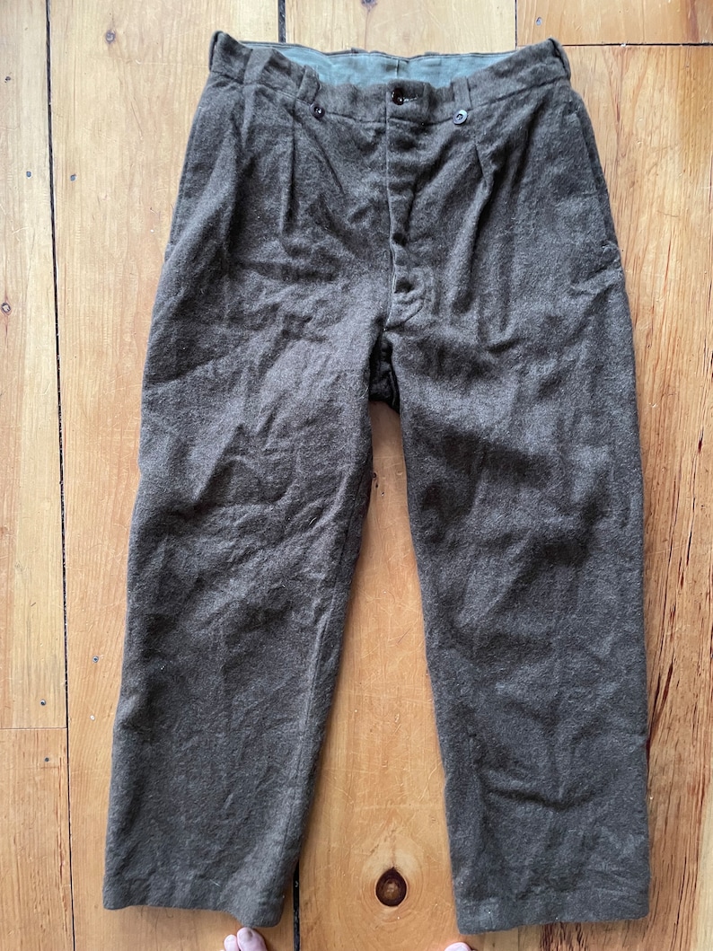 Peut inclure: Un pantalon en laine marron avec une braguette &agrave; boutons et des plis. Le pantalon a une ceinture vert fonc&eacute;.