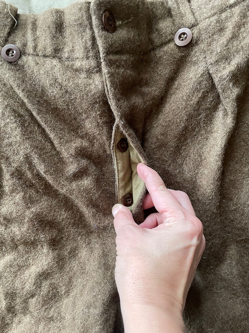 Peut inclure: Gros plan sur l'avant d'un pantalon en laine marron avec une braguette &agrave; boutons. Les boutons sont en plastique marron.