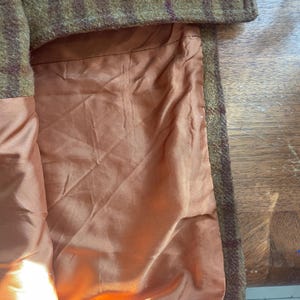 May include: Close-up of the inside of a brown and green plaid coat. The lining is a solid orange color.