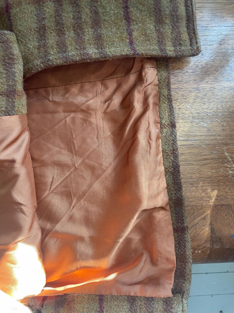 May include: Close-up of the inside of a brown and green plaid coat. The lining is a solid orange color.
