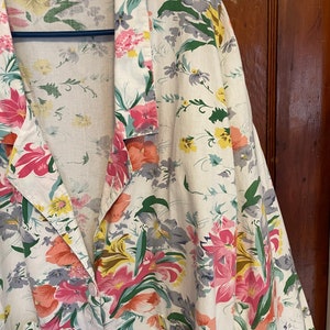 May include: A white button-up shirt with a floral print featuring pink, yellow, and green flowers. The shirt has a collar and long sleeves.