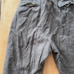 Peut inclure: Un pantalon en laine gris avec deux poches arri&egrave;re. Les poches sont doubl&eacute;es de vert.