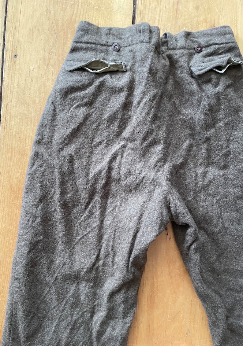 Peut inclure: Un pantalon en laine gris avec deux poches arri&egrave;re. Les poches sont doubl&eacute;es de vert.