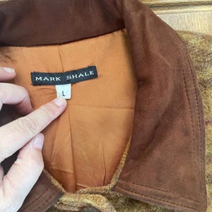 May include: A brown suede jacket with a brown and yellow plaid pattern. The jacket has a brown suede collar and a single button closure. The label on the jacket reads "Mark Shale" and "L".