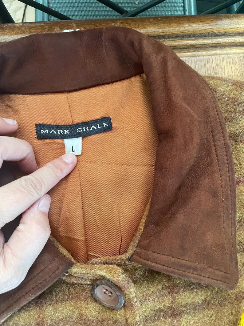 May include: A brown suede jacket with a brown and yellow plaid pattern. The jacket has a brown suede collar and a single button closure. The label on the jacket reads "Mark Shale" and "L".