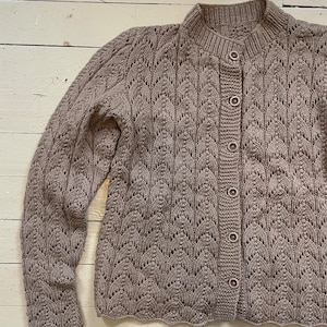 May include: A brown knitted cardigan with a button-up front and a scalloped hem. The cardigan has a delicate openwork pattern.