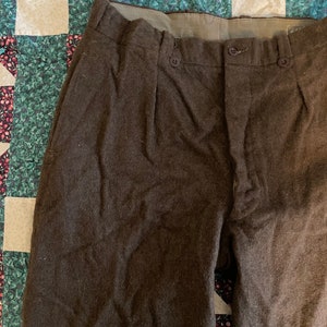 Peut inclure: Un pantalon en laine marron avec une braguette &agrave; boutons et des plis. Le pantalon a une ceinture marron et est fait d'un tissu &eacute;pais et textur&eacute;.