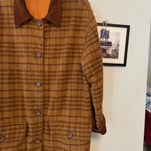 May include: A long brown and red plaid coat with a brown suede collar. The coat has a button closure and two front pockets.