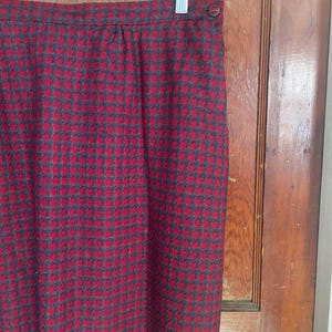 May include: A red and black plaid skirt with a button closure. The skirt is made of a thick, textured fabric.
