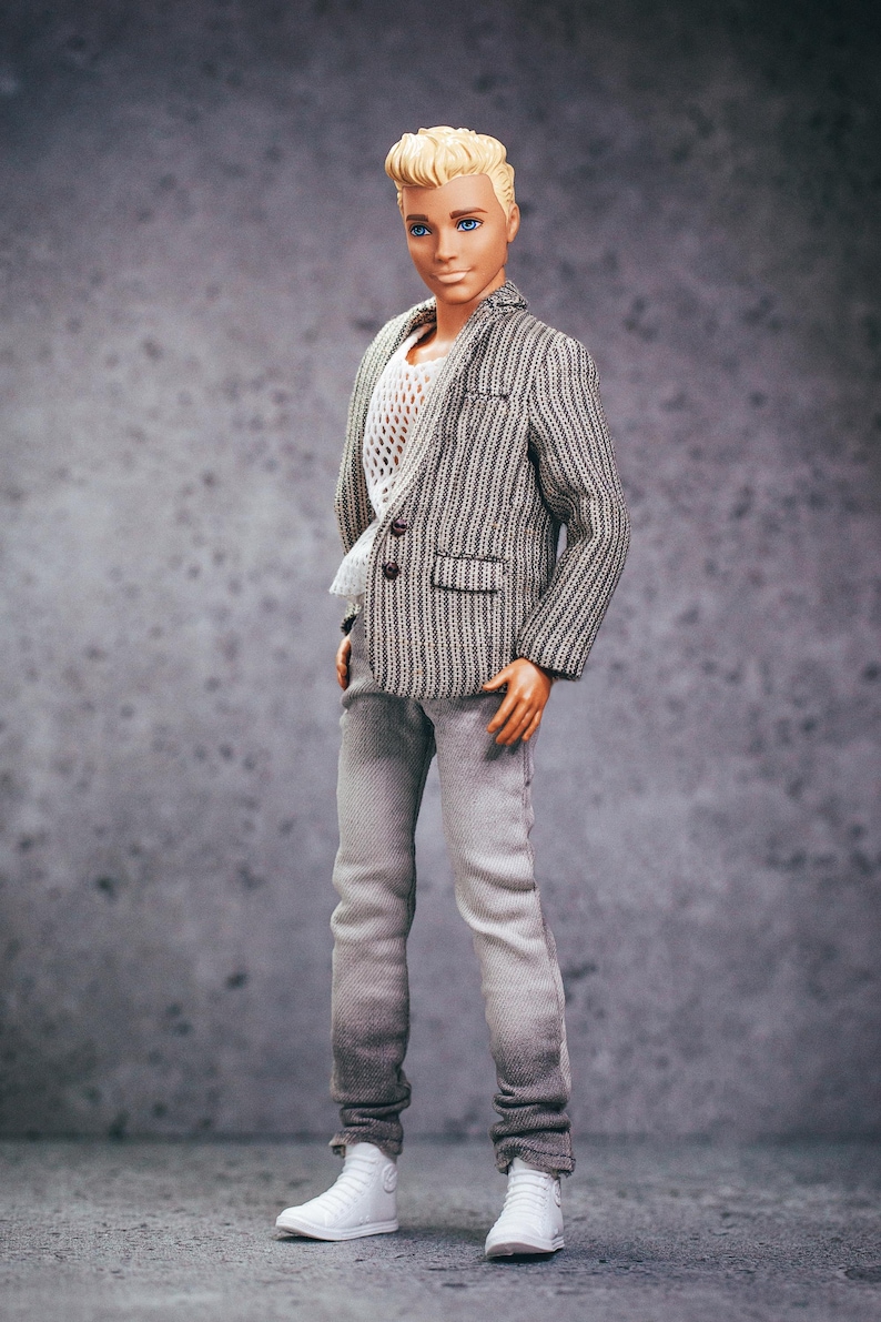 May include: A doll wearing a gray and white striped blazer, white mesh shirt, gray jeans, and white sneakers. The doll has blond hair and blue eyes. The outfit is a modern, casual style.