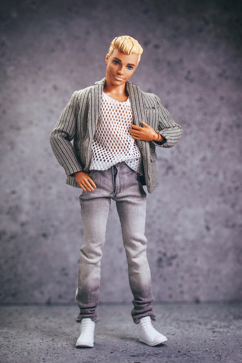 May include: A doll wearing a gray and white striped blazer over a white mesh top, gray jeans, and white sneakers. The doll has blonde hair and blue eyes. The jeans have a faded effect at the bottom.