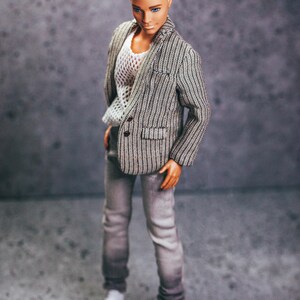 May include: A doll wearing a gray and white striped blazer, a white mesh top, gray jeans, and white shoes. The doll has short, blond hair and is posed against a gray background.