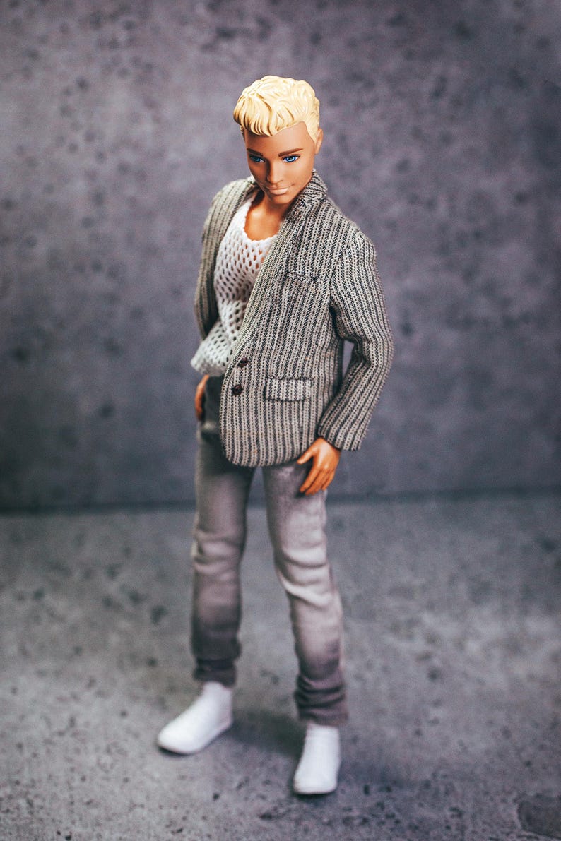 May include: A doll wearing a gray and white striped blazer, a white mesh top, gray jeans, and white shoes. The doll has short, blond hair and is posed against a gray background.