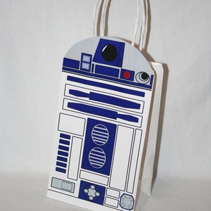 Könnte beinhalten: Eine weiße Papiertüte mit einem blauen und weißen R2-D2-Design. Die Tasche hat einen weißen Papiergriff.