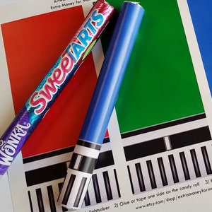Może przedstawiać: Czerwono-biało-niebieski rulon cukierków z nadrukiem "Wonka" i "Sweetarts". Rulony cukierków leżą obok niebiesko-białego ręcznie robionego miecza świetlnego. Tekst na papierze brzmi: "lightsaber 2) Glue or tape one side on the candy roll 3) Roll around www.etsy.com/shop/extramoneyformommy"