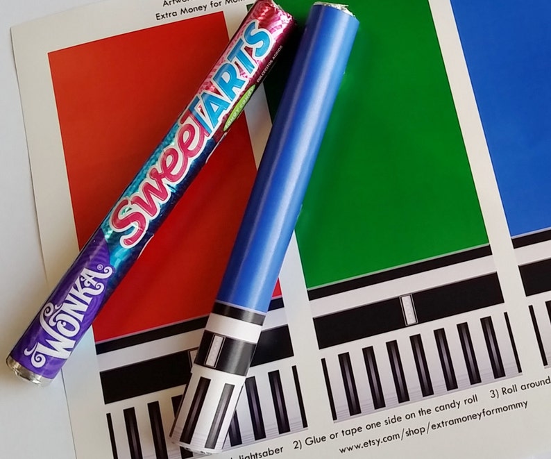 May include: A red, white, and blue candy roll with the words "Wonka" and "Sweetarts" printed on it. The candy roll is next to a blue and white lightsaber craft. The text on the paper reads "lightsaber 2) Glue or tape one side on the candy roll 3) Roll around www.etsy.com/shop/extramoneyformommy"