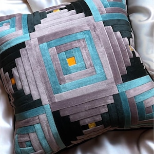 Könnte beinhalten: Quadratisches Zierkissen mit einem geometrischen Muster in Grau-, Türkis-, Schwarz- und Orangetönen. Das Kissen hat eine weiche, samtige Textur und einen schwarzen Rand. Das Design zeigt eine Reihe von geschichteten Rechtecken, die einen modernen, abstrakten Look erzeugen.
