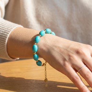May include: A turquoise beaded bracelet with gold-coloured accents. The bracelet features oval-shaped turquoise beads separated by small gold-coloured beads. The adjustable chain is also gold-coloured.