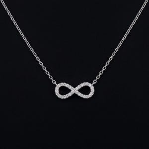 Peut inclure: Un collier de couleur argentée avec un pendentif central en forme de symbole infini. Le charme infini est incrusté de petites pierres claires et scintillantes sur toute sa surface, suspendu à une fine chaîne en métal argenté assortie.