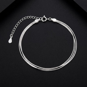 Puede incluir: Una pulsera de varias hebras en tono plateado con tres cadenas finas y lisas conectadas a un cierre de resorte circular. Una cadena extensora adjunta con un pequeño dije plano en forma de gota permite ajustar la longitud de esta joya.