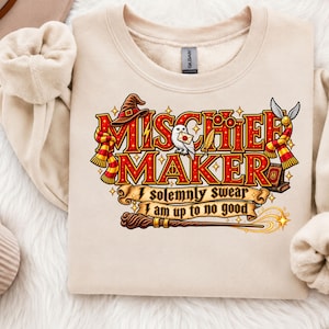 May include: A beige crewneck sweatshirt featuring a graphic print with the text "MISCHIEF MAKER" and "I solemnly swear I am up to no good." The design includes a brown wizard hat, a white owl, a red and yellow scarf, a wand, and a golden snitch.