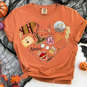 May include: An orange short-sleeve t-shirt featuring a graphic print of various magical icons arranged in a heart shape, including a sorting hat, a golden snitch, a castle, a wand, a broomstick, glasses, and text reading HP, Always, and It's Leviosa not LeviosA.