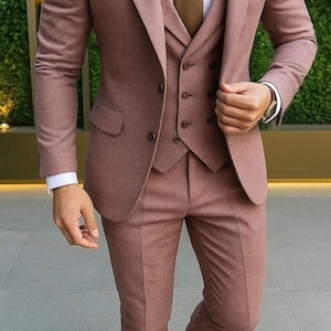 May include: A three-piece suit in a muted rose color, featuring a tailored jacket, vest, and trousers. The suit is paired with a white dress shirt and a brown tie. Brown leather dress shoes complete the ensemble.