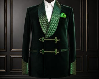 May include: A dark green velvet blazer featuring a quilted shawl collar, matching quilted cuffs, and two horizontal frog closures. The jacket is worn over a crisp white collared shirt and includes a bright green pocket square in the chest pocket.