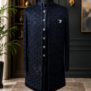 Könnte beinhalten: Ein dunkelblauer Sherwani mit Stehkragen, langen Ärmeln und einer vorderen Knopfleiste mit sechs verzierten silberfarbenen Knöpfen. Das Kleidungsstück ist mit einem komplexen, tonalen geometrischen Muster versehen und enthält ein Einstecktuch.