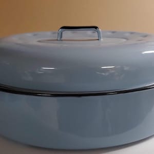 Puede incluir: Una asadera de esmalte azul claro con tapa a juego. La sartén tiene un borde y asas negros, y un asa cromada en la tapa. Esta batería de cocina es adecuada para asar carnes y verduras.