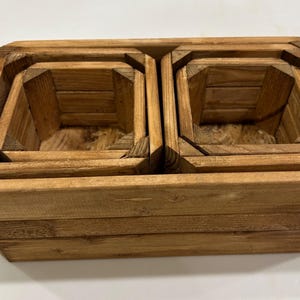 May include: A set of four wooden nesting planters. The planters are square with angled sides and a natural wood finish. The largest planter is at the bottom, with smaller planters nested inside.