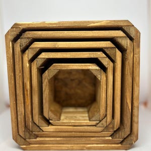 May include: A set of five square wooden planters, designed to nest inside each other. The planters are made from light brown wood. The design is simple and rustic, suitable for gardens or indoor spaces. The planters are of varying sizes.