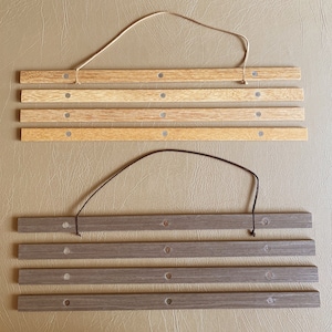 Puede incluir: Dos marcos de fotos de madera con cordones para colgar. El marco superior es de madera marrón claro con cinco listones horizontales. El marco inferior es de madera marrón oscuro con cuatro listones horizontales.