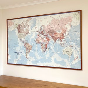 May include: A large framed world map with a dark brown wooden frame. The map shows the world's continents and oceans, with countries in different colors. The words "THE WORLD" are printed at the bottom of the map.