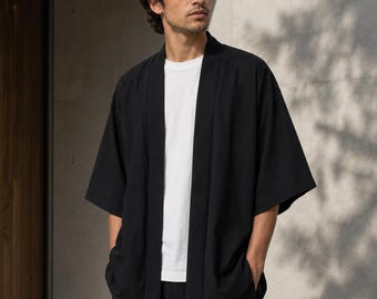 May include: A black open-front kimono-style jacket with wide three-quarter length sleeves, worn over a plain white crew-neck t-shirt. The jacket features a simple, unfastened design with a straight hemline and a smooth, solid black fabric finish.