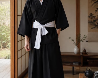 May include: A black two-piece outfit consisting of a long-sleeved wrap-style top with a V-neckline and wide-leg trousers. The ensemble is secured at the waist with a wide, plain white fabric sash tied in a knot at the front, paired with black sandals.