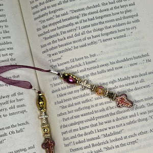 May include: Two bookmarks featuring deep burgundy ribbon attached to metal findings. Each bookmark includes a series of beads in gold, metallic bronze, and clear tones, accented by small silver-toned cross charms and a larger, reddish-brown cross pendant.