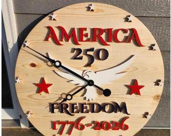 Puede incluir: Un reloj de pared redondo de madera con el texto "AMERICA 250" en rojo y azul. El reloj presenta un águila blanca con las alas extendidas, estrellas rojas y la palabra "FREEDOM" en azul. Las manecillas del reloj son negras.
